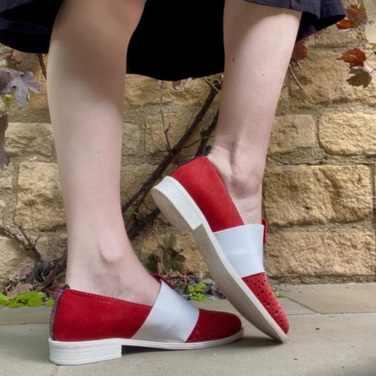 Red and white shoes worn by a person standing on a stone path with a stone wall background.