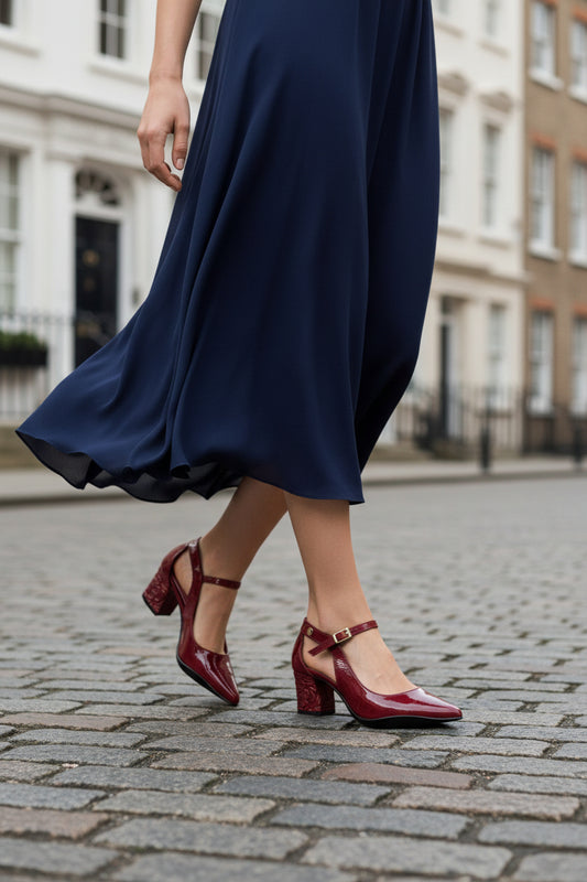 Person wearing a navy blue dress and red shoes on a street.