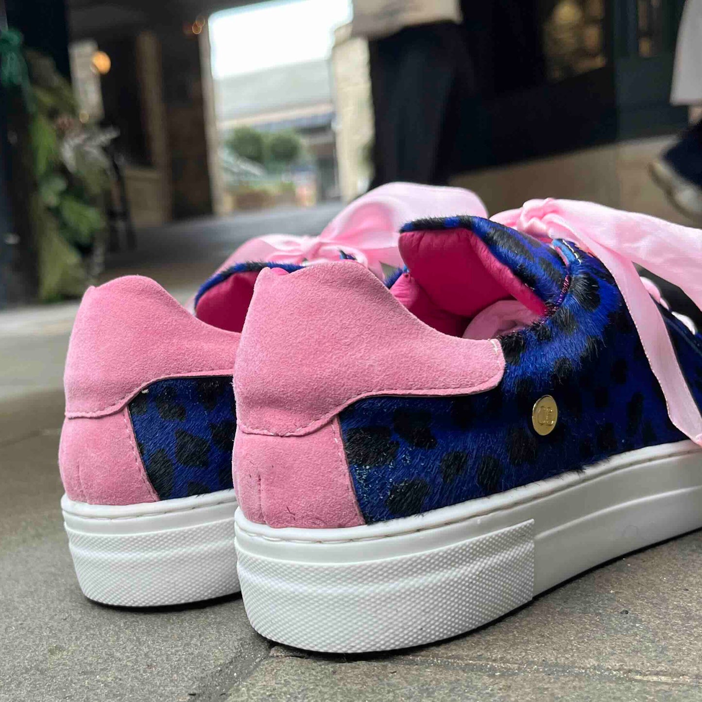 Pink and blue sneakers with a bow on a pavement.