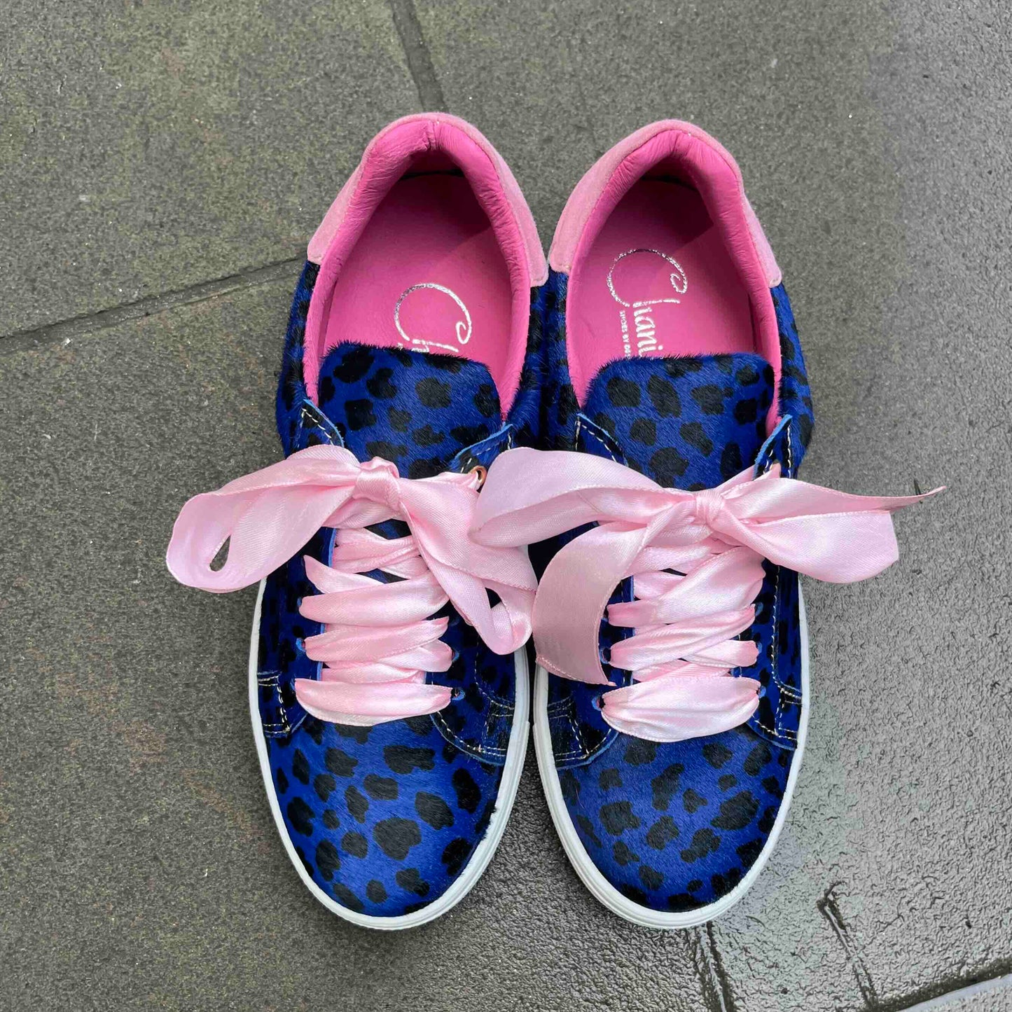 Blue sneakers with pink leopard print accents on a gray pavement