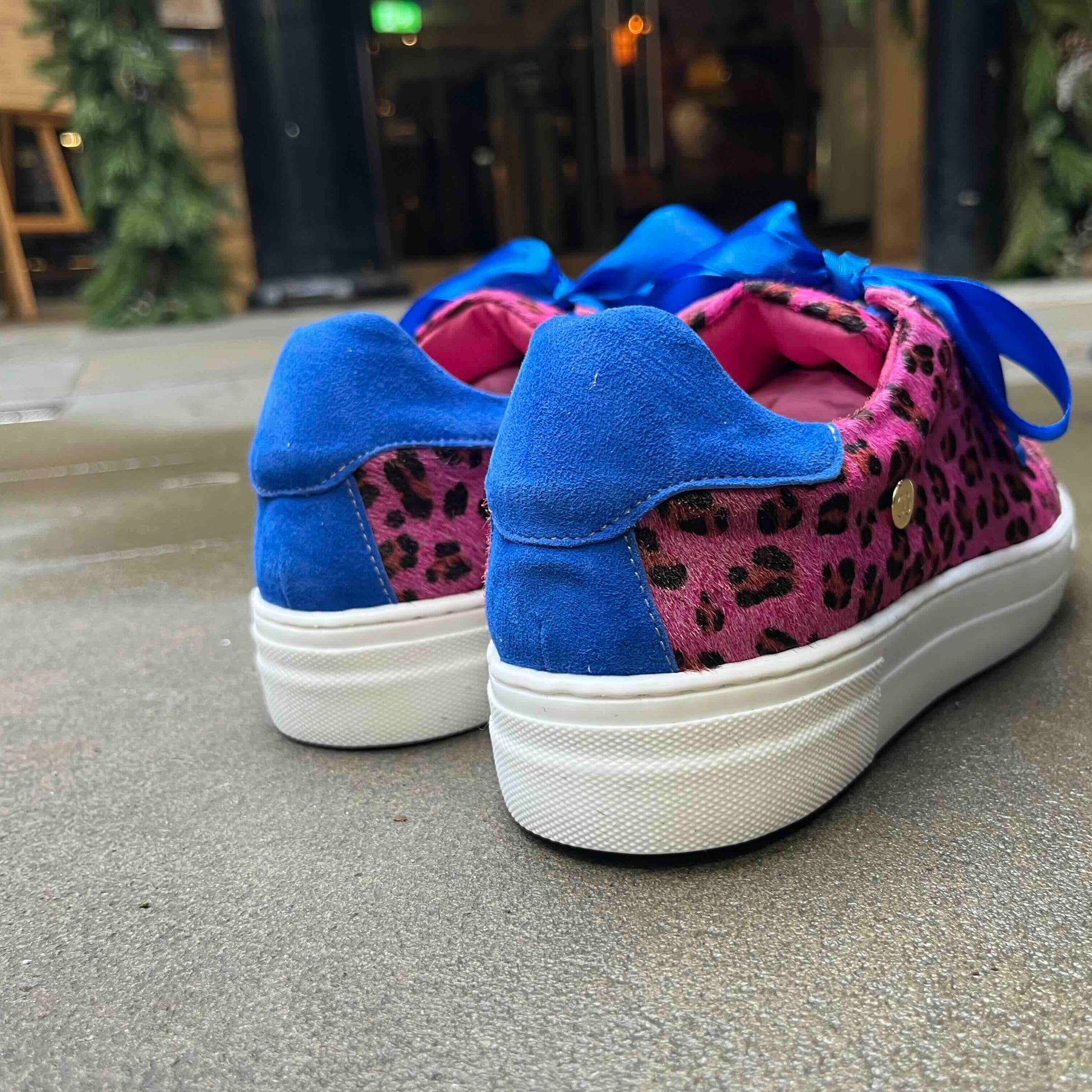 Blue sneakers with pink leopard print soles on a concrete surface.
